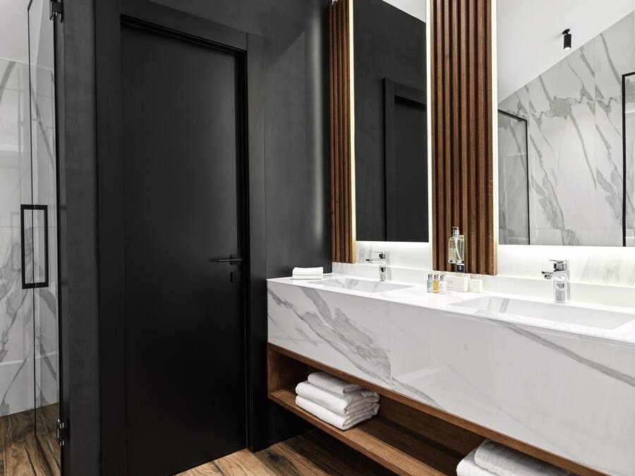 A modern bathroom with a dark door, a large mirror, and a marble countertop.