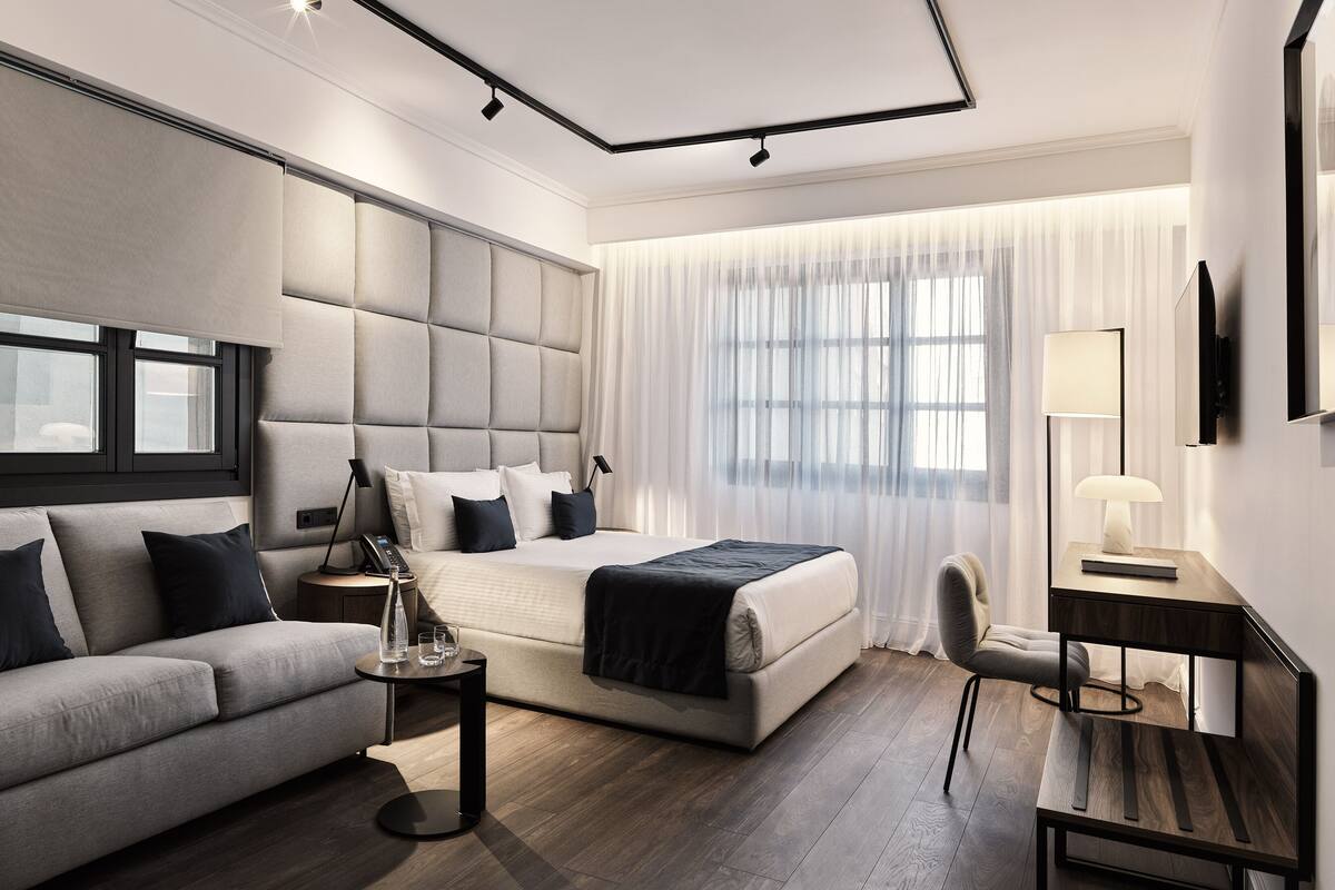 A modern hotel room with a large bed, a sofa, a desk, and a chair.