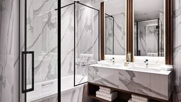 Un baño moderno con paredes de mármol, cabina de ducha de vidrio, tocador de madera con dos lavabos y un espejo grande.