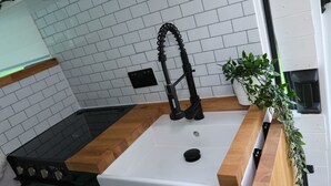 A kitchen with a white sink, black faucet, and wooden countertop. - Superb 4 Berth Campervan With Kingsize bed (Stockton-on-Tees)