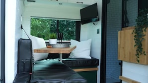 A compact living space with a sofa, a small table with a plant, and a TV mounted on the wall. - Superb 4 Berth Campervan With Kingsize bed (Stockton-on-Tees)
