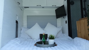 A bed with white bedding, two white pillows, a tray with a green bottle and a black bottle, and a small potted plant. - Superb 4 Berth Campervan With Kingsize bed (Stockton-on-Tees)