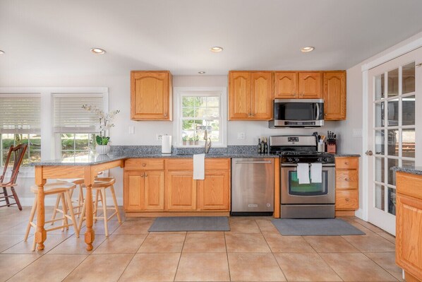 A modern kitchen with wooden cabinets, stainless steel appliances, and a large window.