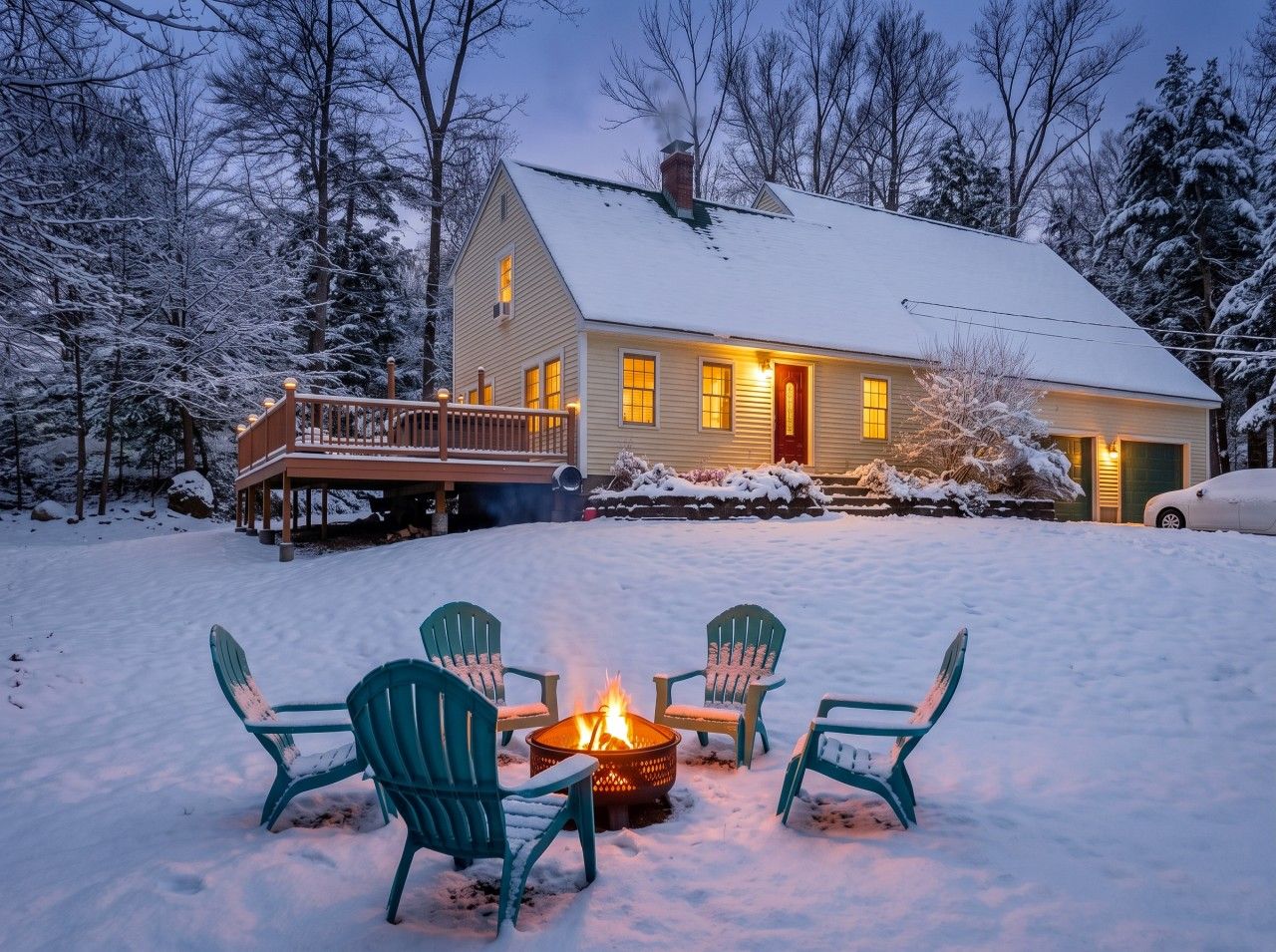 A house with a deck, a fire pit with chairs, and a snowy landscape.