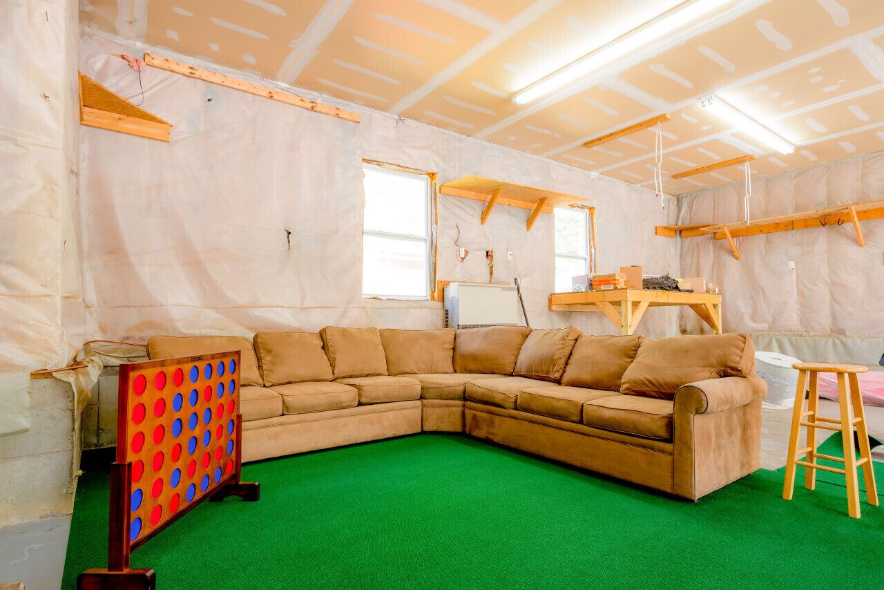 A room with a green carpet, a beige sectional sofa, and a wooden ladder.