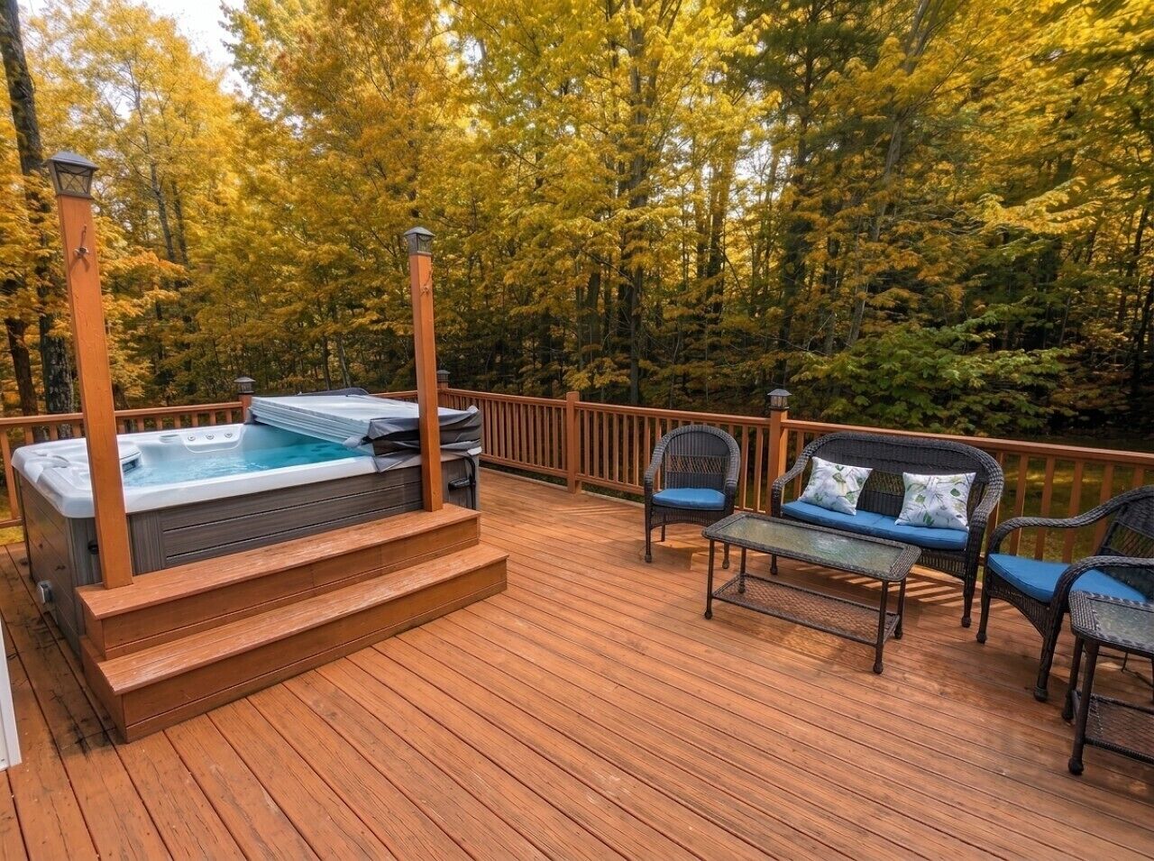 A wooden deck with a hot tub, outdoor furniture, and a view of a forest.