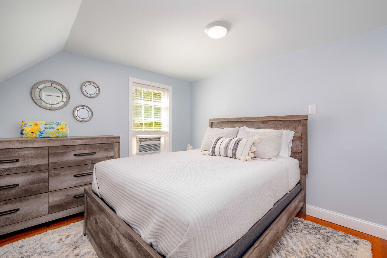 A bedroom with a wooden bed, a dresser, and a window with blinds.
