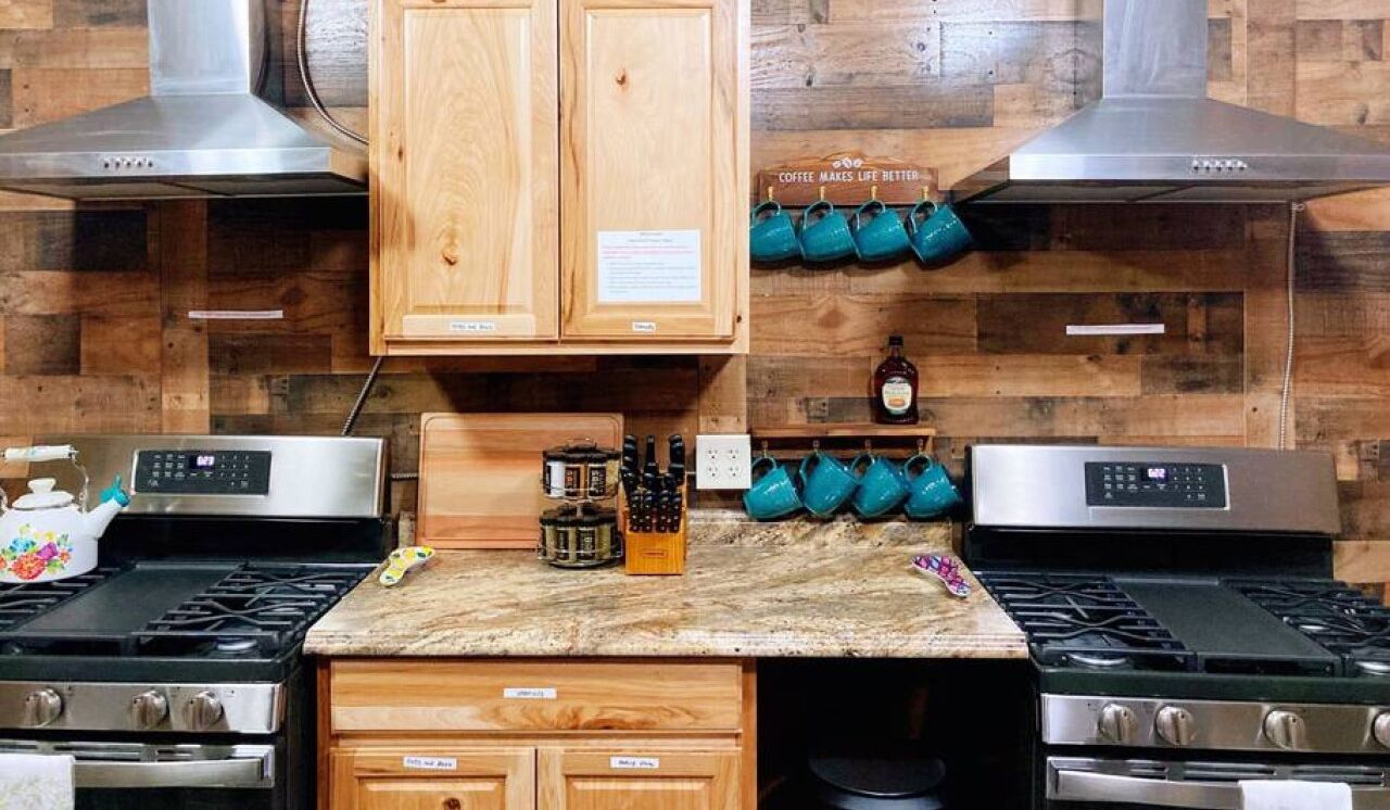 A kitchen with two gas stoves, wooden cabinets, a coffee station, and a stainless steel range hood.
