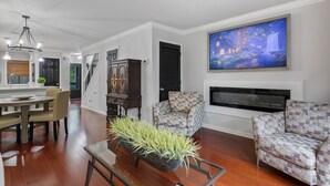 Una sala de estar con chimenea, un televisor montado encima y un comedor con una mesa y sillas de madera.