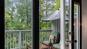 Una terraza de madera con una silla y una mesa, un área de estar cubierta y vistas a árboles.