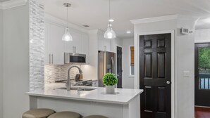 Una cocina moderna con armarios blancos, electrodomésticos de acero inoxidable y una isla central con taburetes.