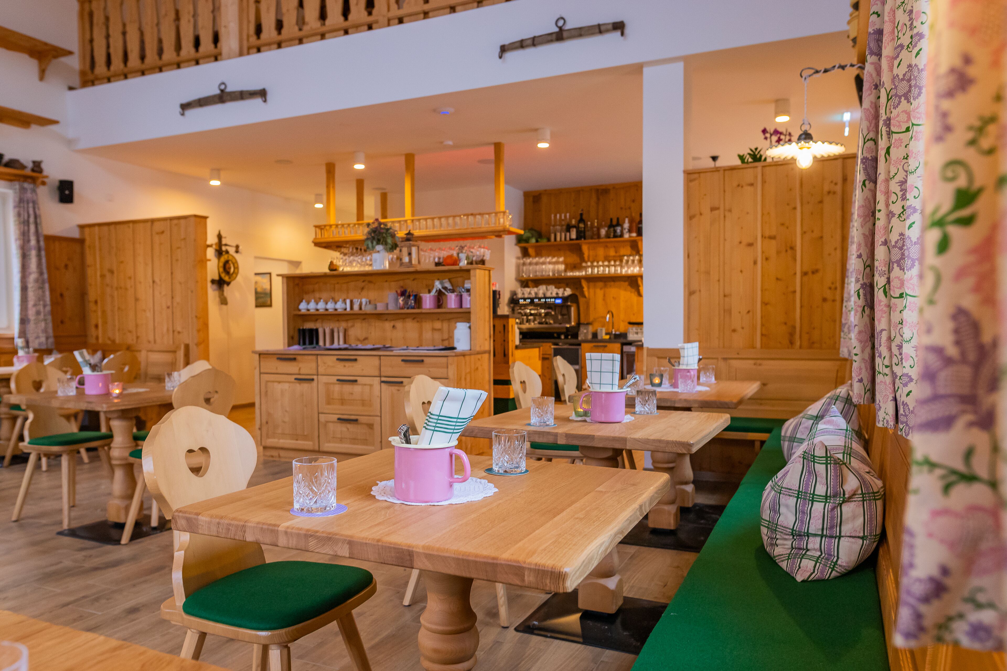 A cozy restaurant with wooden furniture, a bar area, and a green cushioned seating area.