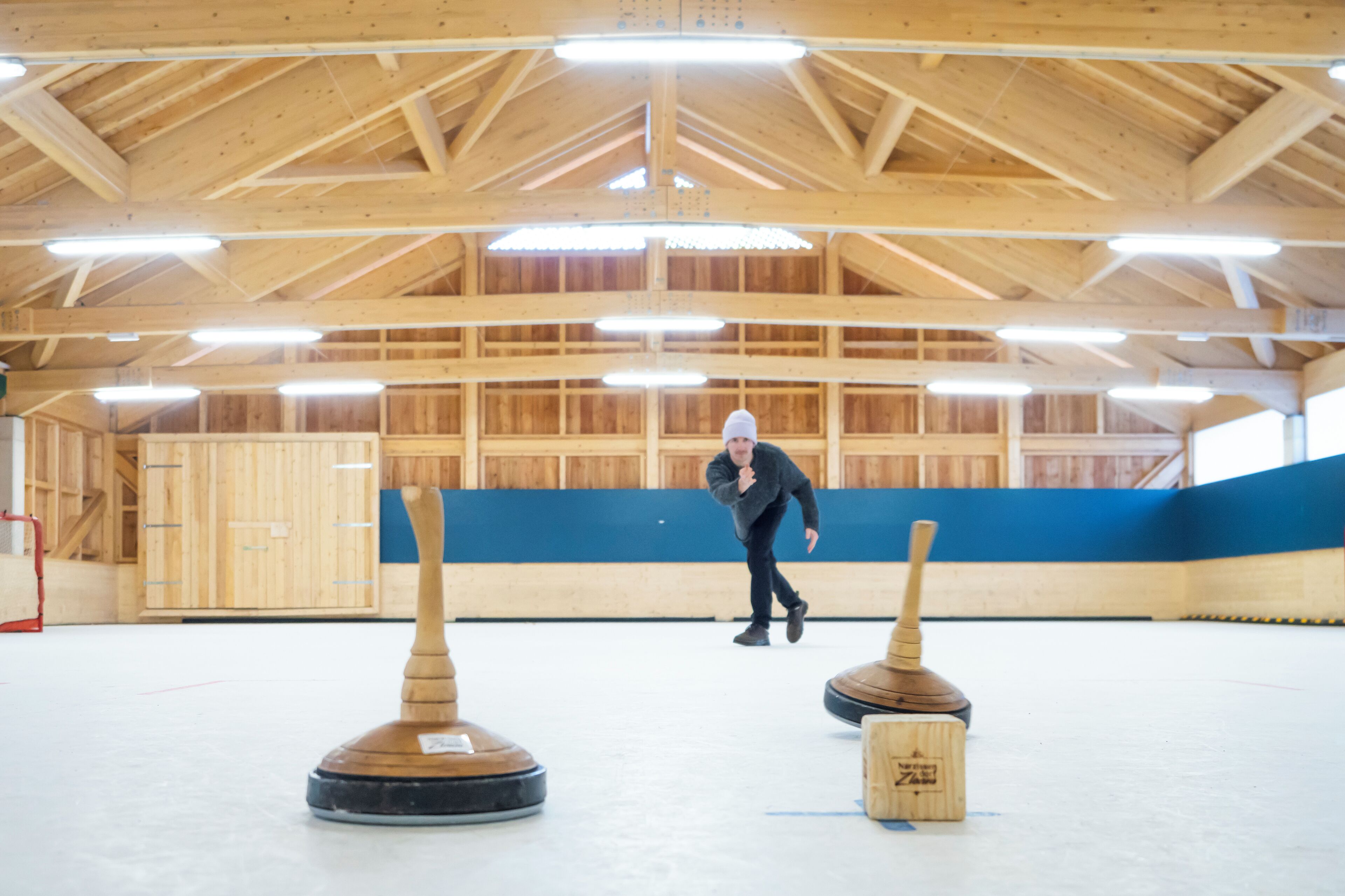 Uma pista de curling interior com paredes de madeira e teto alto.