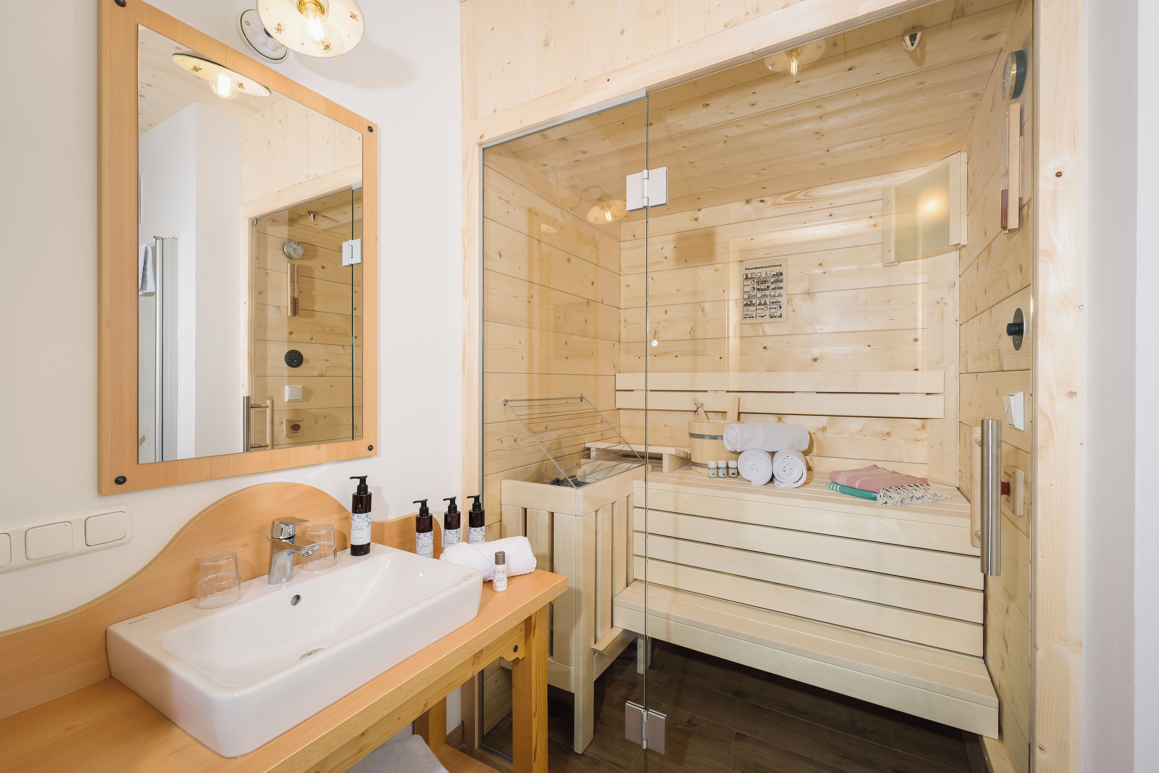 Une salle de bain de style cabane en bois, dotée d’un grand miroir, d’un lavabo et d’une douche séparée par des parois en verre.