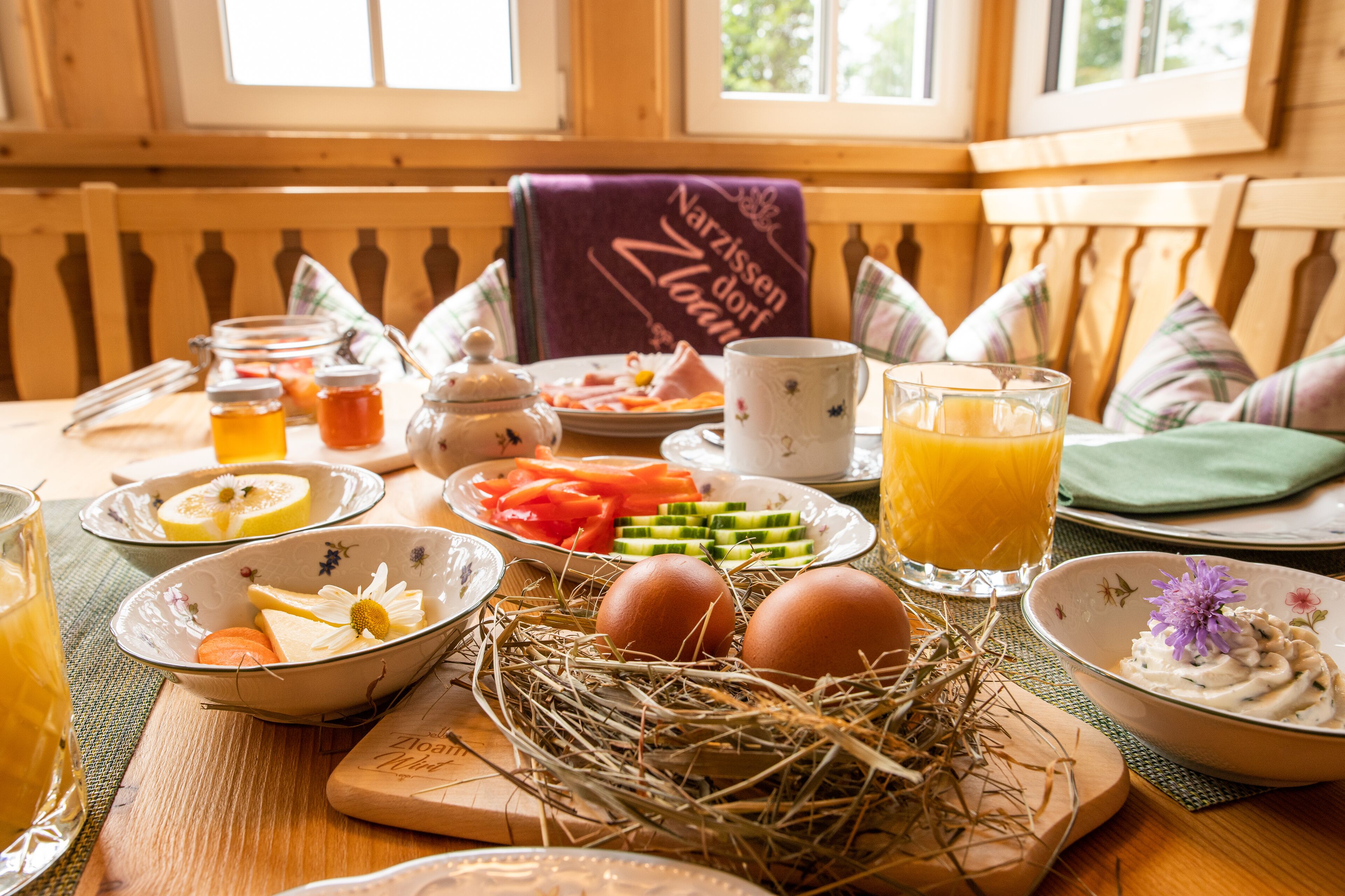Une table de petit-déjeuner avec une table en bois, des assiettes remplies de nourriture, un verre de jus d’orange et un bol d’œufs.