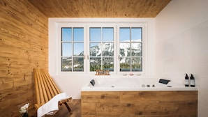 Un ba ño con banco de madera, una bañera grande y una ventana con vistas a la montaña.