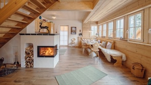 Amplia sala de estar con chimenea, escalera de madera y comedor con banco.