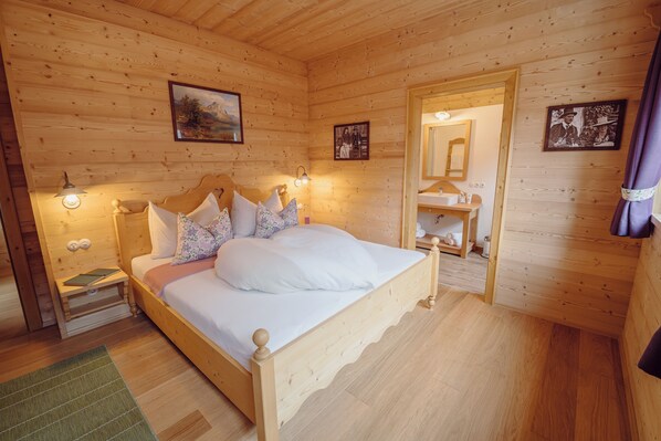 Un dormitorio con paneles de madera, una cama, mesitas de noche, lámparas fijadas a la pared y cuadros enmarcados.