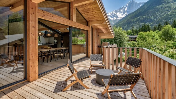 A wooden deck with outdoor seating and a view of mountains. - Chic & Spacious Chalet with Hot Tub & Sauna (Chamonix-Mont-Blanc)
