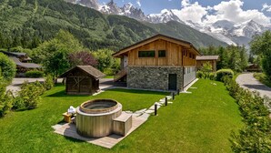A wooden chalet with stone walls, a hot tub, and a view of snow-capped mountains. - Chic & Spacious Chalet with Hot Tub & Sauna (Chamonix-Mont-Blanc)