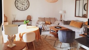 A living room with a round table, a sofa, a coffee table, and a large wall clock. - 🌊 Ti Glaz - Île-Tudy – A charming home between the sea and the river (Île-Tudy)