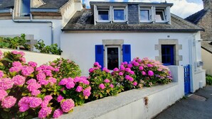 A white building with blue shutters, a small balcony, and pink flowers in front. - 🌊 Ti Glaz - Île-Tudy – A charming home between the sea and the river (Île-Tudy)