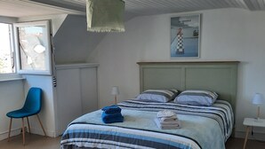 A bedroom with a bed, a chair, a lamp, and a painting on the wall. - 🌊 Ti Glaz - Île-Tudy – A charming home between the sea and the river (Île-Tudy)