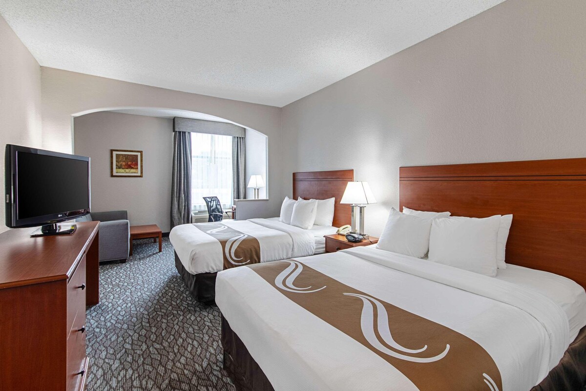 Habitación de hotel con dos camas, televisión, escritorio y ventana con cortinas.
