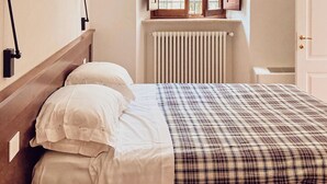 Ein Schlafzimmer mit einem Holz-Kopfteil, zwei Nachttischlampen, einer karierten Bettdecke, einem Fenster mit Holzjalousien und einer Heizung.