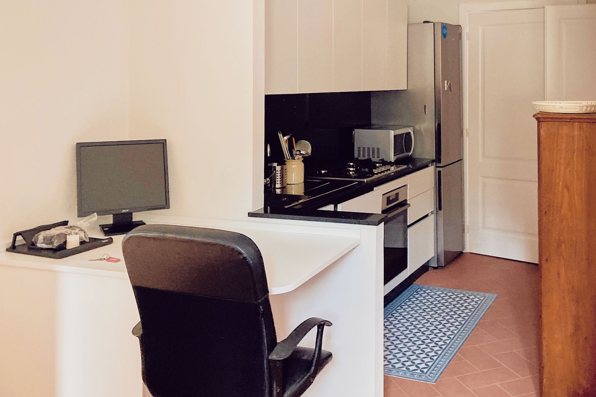 Eine kleine Küche mit Kühlschrank, Mikrowelle und Herd. Es gibt eine kleine Essecke mit einem Stuhl und einem Tisch.
