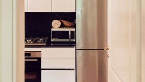 Eine kompakte Küche mit weißen Schränken, einem Edelstahl-Kühlschrank, einer Mikrowelle und einem Gasherd.