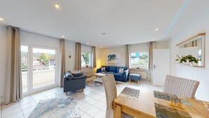 A spacious living room with a blue sofa, a grey armchair, and a wooden dining table. - Vacation apartment in the Harz Mountains - Schulenberg (Schulenberg im Oberharz)