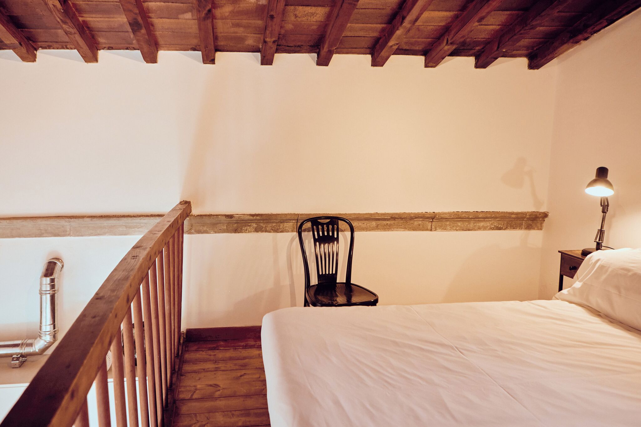 Une chambre avec un plafond en bois, un lit, une chaise et une table de chevet avec une lampe.