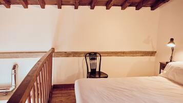 Une chambre avec un plafond en bois, un lit, une chaise et une table de chevet avec une lampe.