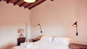 Een slaapkamer met een bed, twee bedlampen, een nachtkastje met lamp en een houten plafond.