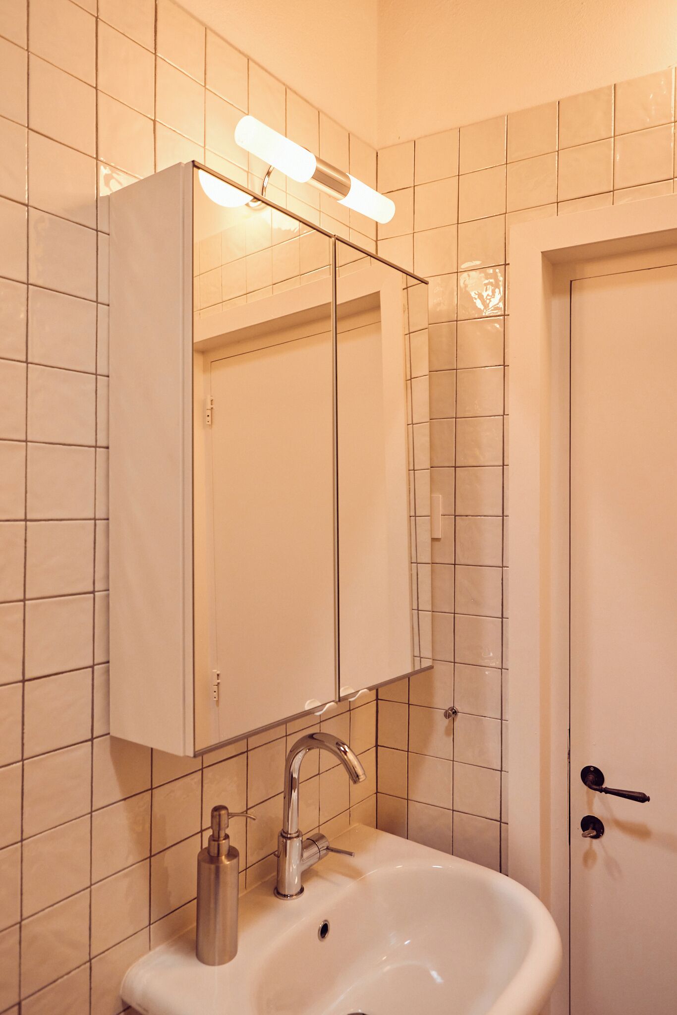 Un baño con un lavabo blanco, un espejo y una puerta.