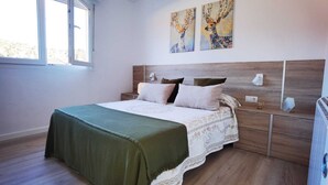 A bedroom with a wooden headboard, a bed with a green blanket, two wall-mounted lamps, and two paintings above the bed. - La Terraza de Alma (O Milladoiro)