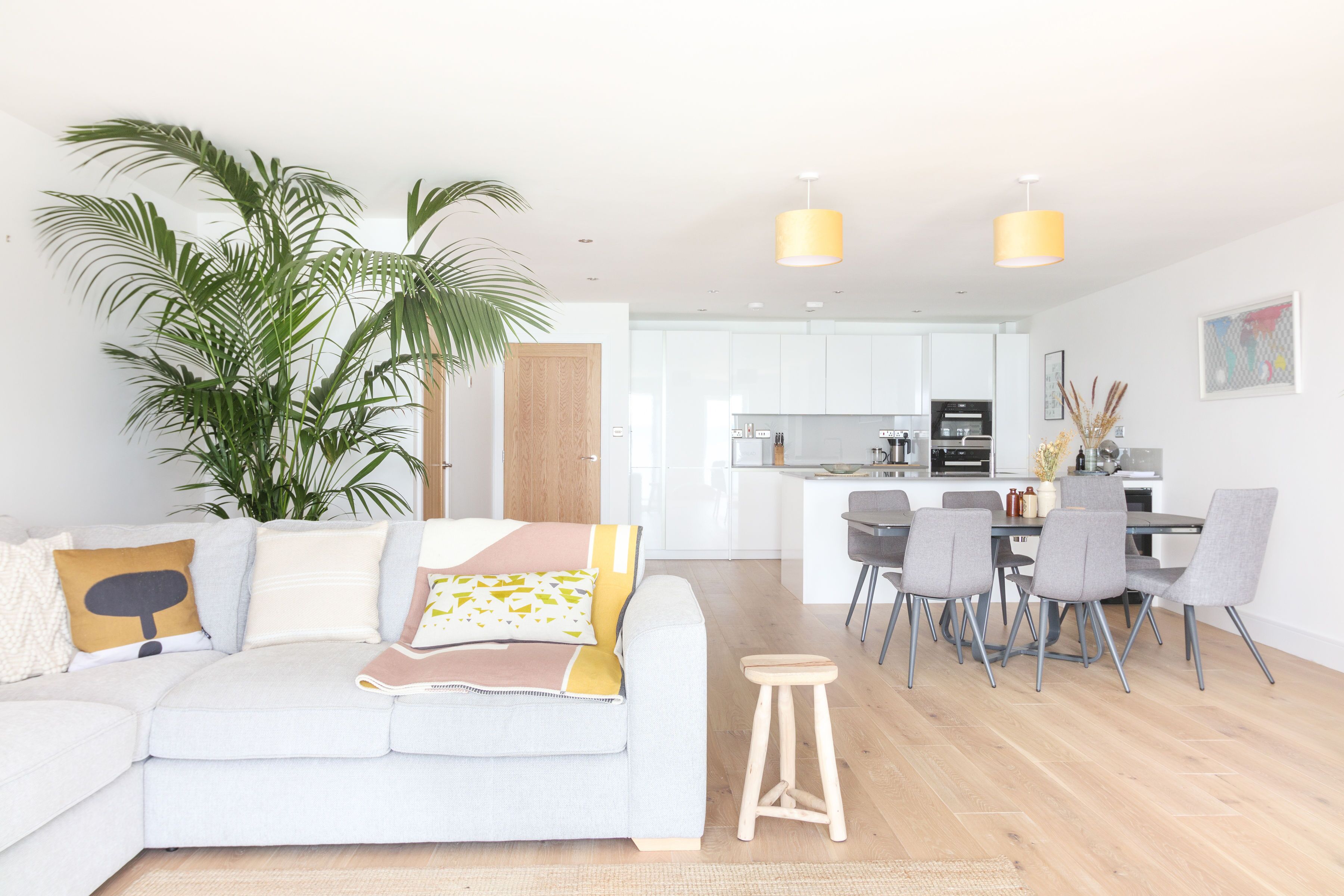 Una sala de estar moderna con un sofá de color claro, un taburete de madera y un comedor con sillas grises y una mesa.