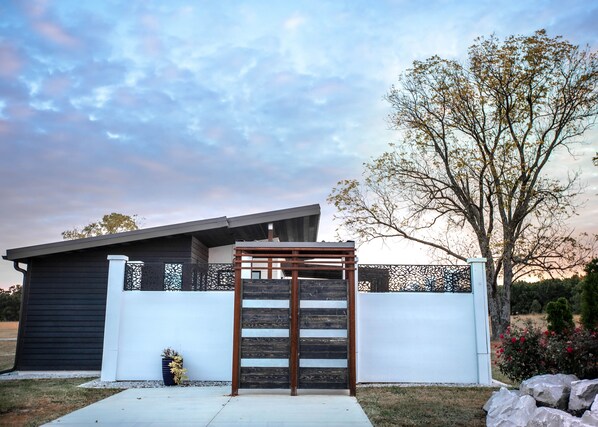 Une maison moderne avec un portail en bois, une clôture noire et un arbre en arrière-plan.
