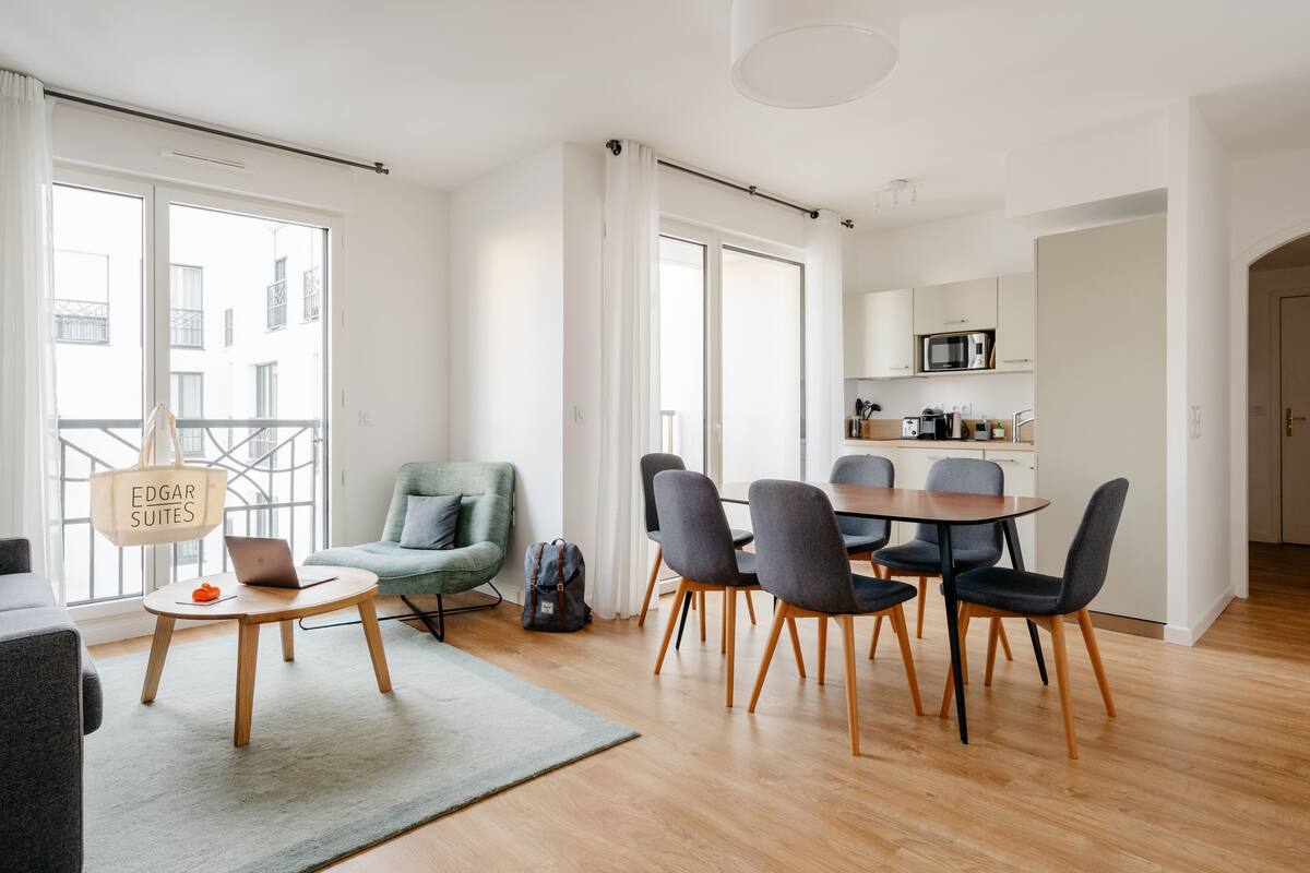 Un salon moderne comprenant un coin repas, un canapé, un fauteuil et une table avec un ordinateur portable.