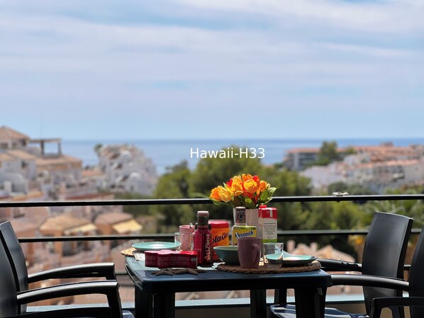 A table with a view of a coastal town, a vase of flowers, and various items including a bottle of Arizona water, a Nescafé mug, and a glass.