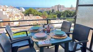 Mesa en balcón con platos, vasos y una botella, con vista a una ciudad costera.