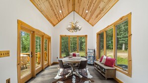 A spacious room with a large wooden ceiling, a round table with chairs, a chandelier, and large windows offering a view of the outdoors. - Cabin, Pool, Hot Tub, Wineries and Mountains Oh My! (Culpeper)