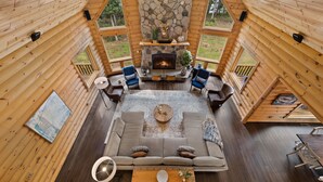 A cozy cabin interior with a stone fireplace, wooden walls, and a large sofa in the center. - Cabin, Pool, Hot Tub, Wineries and Mountains Oh My! (Culpeper)