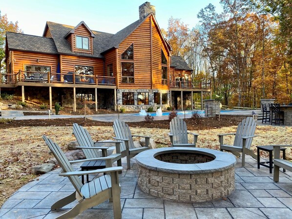 A log cabin with a stone fireplace, outdoor seating, and a swimming pool.