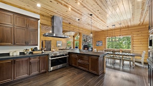 A modern kitchen with wooden cabinetry, a large island, and a stone accent wall. - Cabin, Pool, Hot Tub, Wineries and Mountains Oh My! (Culpeper)