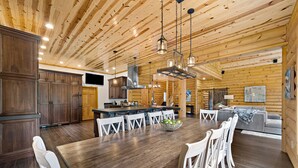 A spacious kitchen with a large island, wooden ceiling, and white chairs around a dining table. - Cabin, Pool, Hot Tub, Wineries and Mountains Oh My! (Culpeper)