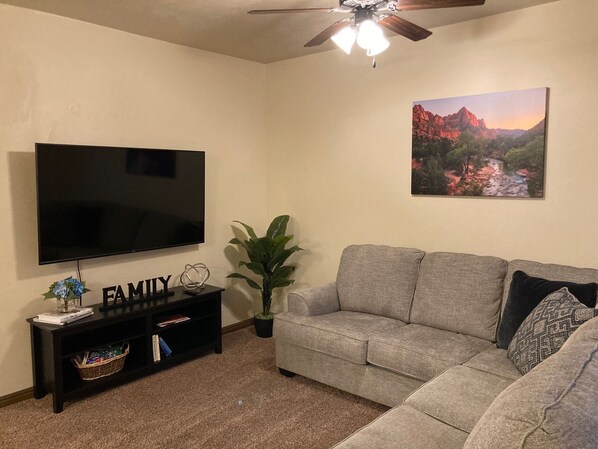 Ein Wohnzimmer mit Flachbildfernseher, einer Couch, einem Deckenventilator, einer Pflanze und einem Bild an der Wand.