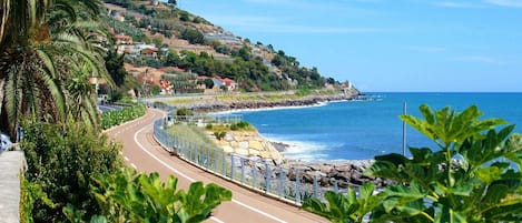 A coastal road with a stone wall and a guardrail, leading to a beach.