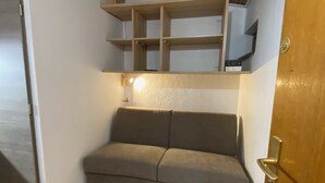 Ein Zimmer mit Holzboden, einem grauen Sofa und eingebauten Regalen.